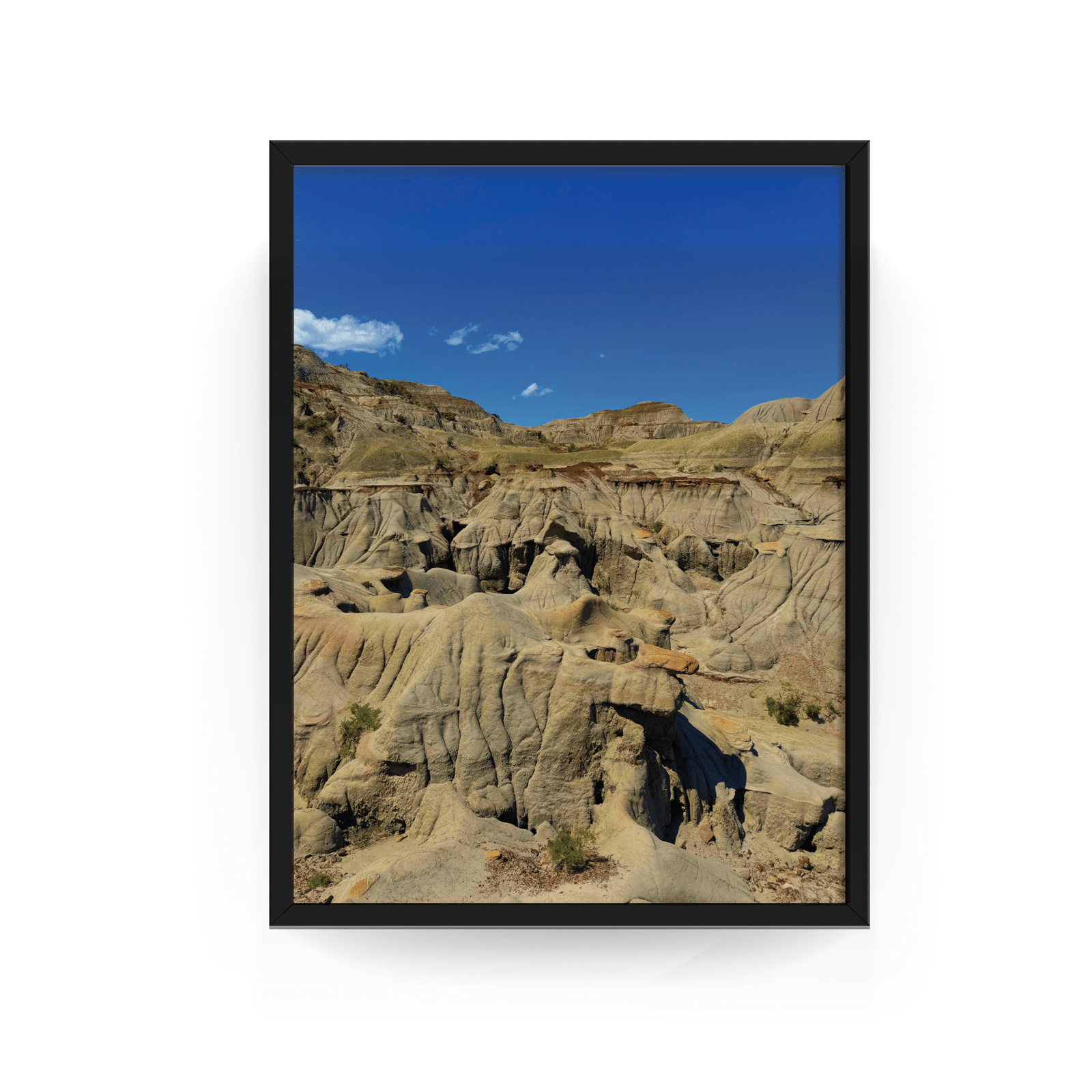 Vertical black-framed photograph of rugged Badlands rock formations at Dinosaur Provincial Park under a bright blue Alberta sky.